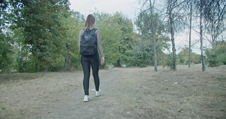 Wall Mural - A young woman with a backpack takes a peaceful stroll through a park, enjoying the fresh air and quiet scenery.