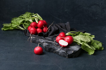 Wall Mural - Wooden board of ripe radish with green leaves on dark background