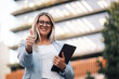 © Zamrznuti tonovi - Businesswoman holding tablet giving thumbs up outside office building