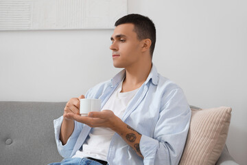 Poster - Handsome young man with cup of coffee resting on sofa in living room