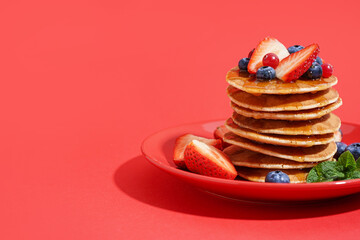 Wall Mural - Plate with tasty pancakes, strawberry and blueberries on red background