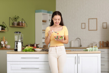 Wall Mural - Beautiful young happy Asian woman with bowl of fresh vegetable salad in kitchen