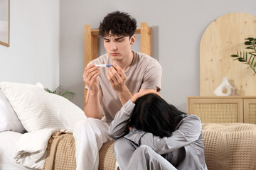 Wall Mural - Sad young couple with pregnancy test in bedroom