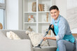 © Pixel-Shot - Young man in apron vacuum cleaning sofa at home
