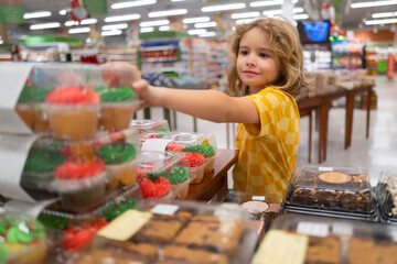 Wall Mural - Kid choosing cakes, cupcake muffin. Portrait of child in a store or a supermarket. Little kid going shopping. Sweet food for kids.