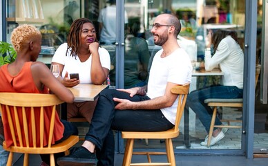 Wall Mural - three diverse friends people sitting at an outdoor cafe, engaged in conversation. casual diverse gro