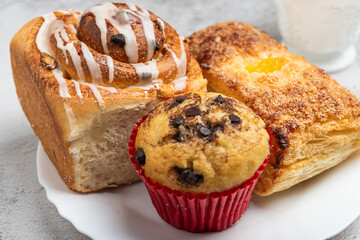 Close-up of a white plate with different freshly baked desserts, cinnamon roll, cupcake, and a sweet pastry.