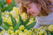 © Volodymyr - A child hold tulip on blossom Spring nature background. Spring flowers. A kid playing in Blossom spring park. Adorable little boy looking at beautiful yellow tulips.