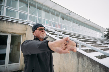 Wall Mural - Senior Man Stretching His Arms Outdoors on Snowy Steps During Winter