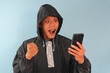 © Lailar Studio - Asian man wearing raincoat holding mobile phone with happy expression
