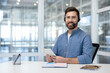 © Liubomir - Video call, man with headset and tablet computer looking at camera. Support worker at workplace advising and helping clients remotely. Office worker inside office.