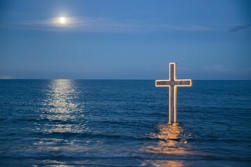 Illuminated cross stands calmly in the ocean under a moonlit sky.