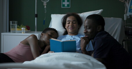 Wall Mural - Young African girl in a hospital room with her parents sitting by the child's side reading a book together.