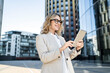 © muse studio - Professional woman using a tablet in a modern city setting on a sunny day