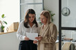 © Clique Images - Two female economists or analysts looking through information on paper document at working meeting