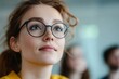 © Sergio - Young woman with glasses listens attentively during a presentation in a bright indoor setting