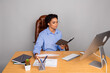 © deagreez - Confident businesswoman working at office desk, holding notebook focused on tasks, surrounded by documents computer on grey background.