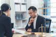 © Kritdanai - Legal Consultation: A serious and focused legal consultation takes place between a male lawyer and his client, shown reviewing important legal documents in a professional office setting.