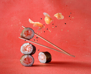 Wall Mural - Classic sushi rolls with pickled ginger and sesame falling down on a red background