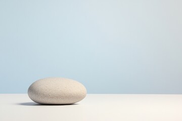 minimalist composition of single smooth stone resting on clean white surface under diffused lighting