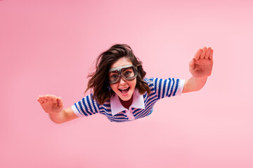 Wall Mural - Joyful young woman with goggles floating against a pink background in trendy striped knitwear