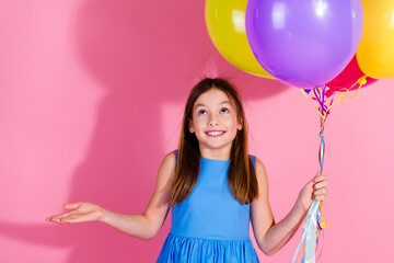 Wall Mural - Happy girl in blue dress holding colorful balloons against pink background, expressing joy and excitement