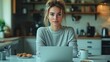 © Kalivmasa - A young woman working on her laptop in her kitchen, with a cup of coffee and some pastries in front of her.