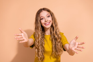 Wall Mural - Smiling young woman in casual wear reaching out towards camera on beige background