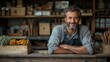© LEELA - Smiling man in apron behind a rustic wooden counter with flowers.