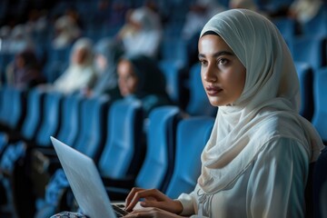 Arab woman in hijab at tech conference using laptop.