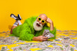 © deagreez - Eccentric elderly man in green fur coat celebrating with cash against a vibrant yellow backdrop