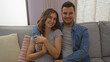 © Krakenimages.com - Man and woman couple sitting together on a couch in a cozy living room indoors, smiling and embracing each other warmly.