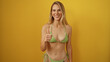© Krakenimages.com - Young woman smiling in a green bikini giving a thumbs up against a yellow background wall