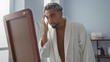 © Krakenimages.com - Young man in a spa wearing a bathrobe, looking into a mirror with hair treatment in a wellness center