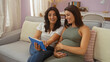 © Krakenimages.com - Mother and pregnant daughter sitting together on a couch at home looking at a tablet with love and smiles