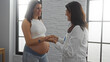 © Krakenimages.com - Pregnant woman smiling during a prenatal appointment with a female doctor in a clinical setting.