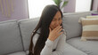 © Krakenimages.com - Woman sitting indoors in a home setting, young asian female with long hair on a comfortable sofa in a cozy living room atmosphere.