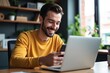 © velikiyzayats - A Smiling Young Man Engaged in Remote Work at a Modern Home Office, Utilizing Technology via Smartphone and Laptop to Stay Connected