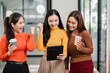© Satori Studio - Three young women cheerfully celebrate while looking at a tablet in a bright, modern office setting.