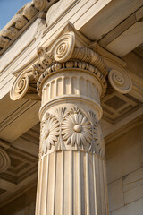 Fototapete - Detailed view of fluted column with ornate capital featuring spiral volutes and floral motifs in beige stone. Close-up showcasing classical architectural craftsmanship. 