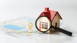© Pojjanee - Miniature house model with magnifying glass over map showing location pin for real estate exploration and investment opportunities