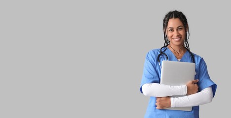 Poster - Young African-American female doctor holding laptop on grey background with space for text