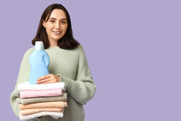 Wall Mural - Young woman with clean towels and bottle of detergent on lilac background