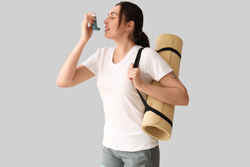 Sticker - Sporty young woman with fitness mat using inhaler on light background