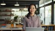 © Chirawan - An Asian woman in her 40s, standing next to her desk with her laptop, ready for a video meeting, in a tidy, well-organized space.