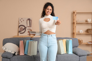 Wall Mural - Happy young African-American woman with shopping bags, laptop and credit card at home