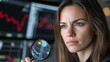 © Phirakhup - A focused woman analyzes stock market data through a magnifying glass.
