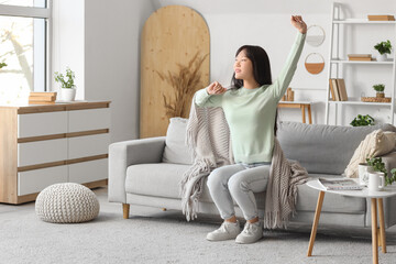 Wall Mural - Young Asian woman with grey plaid stretching on sofa at home