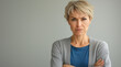 © Anastasiia Havelia - An angry middle-aged woman with short blonde hair stands in front of the camera, her arms crossed and frowning slightly against an isolated gray background. She is wearing a blue t