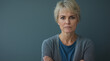 © Anastasiia Havelia - An angry middle-aged woman with short blonde hair stands in front of the camera, her arms crossed and frowning slightly against an isolated gray background. She is wearing a blue t